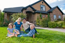 Family sitting in grass in front of newly constructed home.